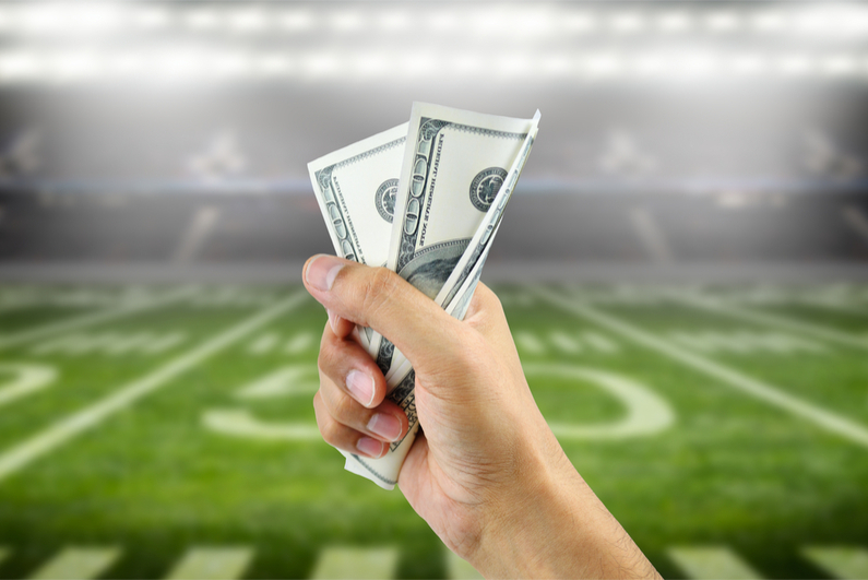 Close up of a man's hand crushing a wad of hundred dollar bills in concept of getting money with bets in American football